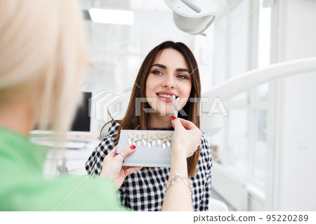 Beautiful young woman at dentist's office choose teeth color tone. 95220289