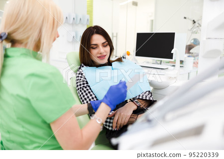 Dental clinic doctor shows a panoramic x-ray picture to his patient. Doctor explains to her patient the condition of her teeth. Dental clinic doctor shows a panoramic x-ray picture to his patient. Doctor explains to her patient the condition of her teeth. 95220339