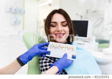 Dentist and his patient choose a tone of veneers. Dentistry doctor shows a palette with shades for teeth. 95220341