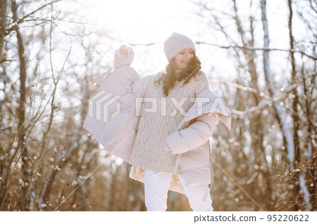 Young woman in winter style clothes walking in the snowy park. Winter fashion, holidays. 95220622