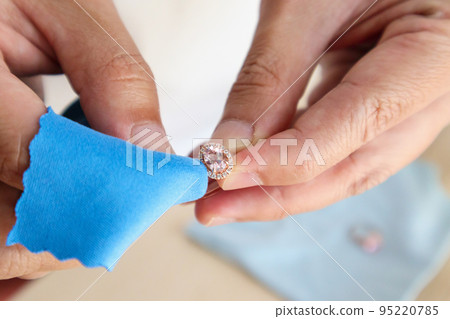 Jeweller hand polishing and cleaning jewelry diamond ring with micro fiber fabric 95220785