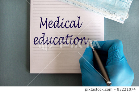 Male doctors hand in blue glove writes the words 'medical education' on a white note. Medicine mask. Beautiful blue background. Male doctors hand in blue glove writes the words 'medical education' on a white note. Medicine mask. Beautiful blue background. 95221074
