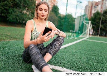 Sports girl sitting on the football field and using the phone Sports girl sitting on the football field and using the phone 95221670