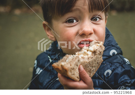 Upset poor hungry kid is eating bread. Homeless with dirty face. Portrait of child boy with big eyes. Crisis, peace, stop aggression, War in Ukraine. Sad refugee. Face asking for food 95221968