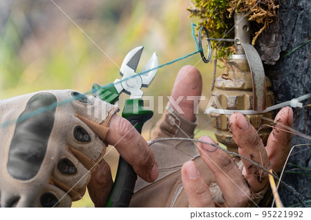 Close-up photo - a sapper clears a booby trap. The wire cutters cutting the wire of the frag grenade trap. Close-up photo - a sapper clears a booby trap. The wire cutters cutting the wire of the frag grenade trap. 95221992