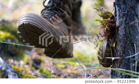 Soldier steps on a mine trap. The soldier's boot rips off the wire and rips off the pin of the grenade. Soldier steps on a mine trap. The soldier's boot rips off the wire and rips off the pin of the grenade. 95221996