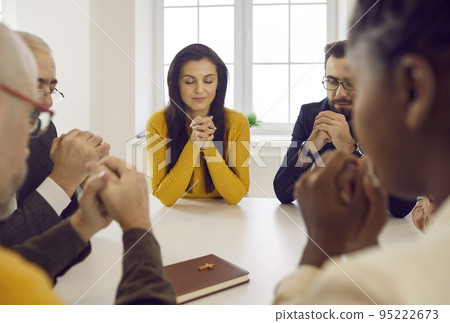 Diverse group of people praying to Lord sitting together around table with Bible Diverse group of people praying to Lord sitting together around table with Bible 95222673