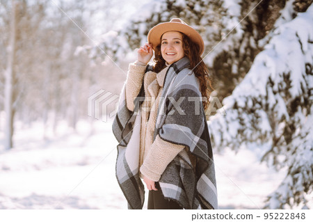Beautiful woman standing among snowy trees and enjoying first snow. Happy winter time. Christmas. 95222848