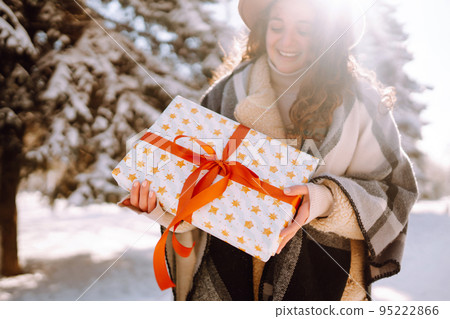 Pretty Woman holding a giftbox with red ribbon in the winter park. Happy winter time. New year's. 95222866