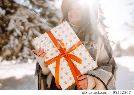 Pretty Woman holding a giftbox with red ribbon in the winter park. Happy winter time. New year's. 95222867