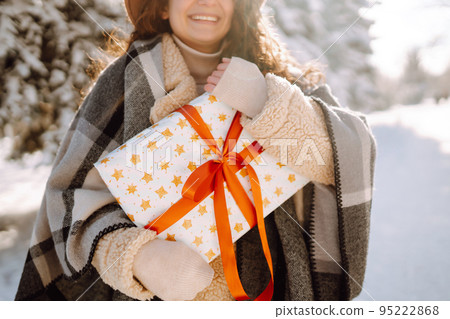Pretty Woman holding a giftbox with red ribbon in the winter park. Happy winter time. New year's. 95222868