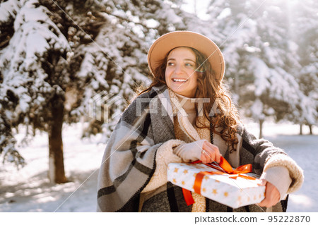 Pretty Woman holding a giftbox with red ribbon in the winter park. Happy winter time. New year's. 95222870
