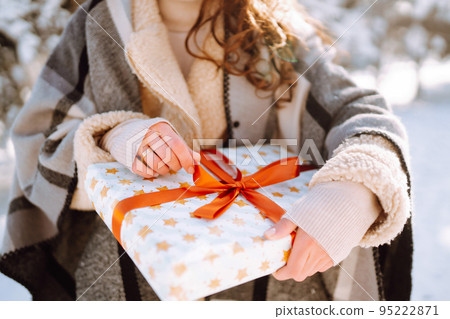 Pretty Woman holding a giftbox with red ribbon in the winter park. Happy winter time. New year's. 95222871