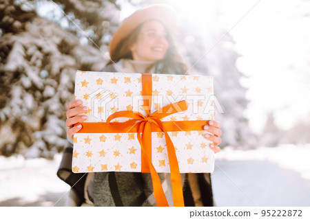 Pretty Woman holding a giftbox with red ribbon in the winter park. Happy winter time. New year's. 95222872
