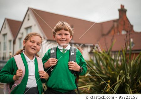 Portrait of school kids boy and girl in green uniform with backpacks near school building. Happy children ready to study. Funny students of primery school. Back to school Portrait of school kids boy and girl in green uniform with backpacks near school building. Happy children ready to study. Funny students of primery school. Back to school 95223158