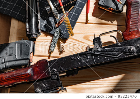 Black disassembled shotgun and cleaning tools on wooden table . 95223470