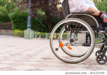 Unrecognizable woman with disability sitting in wheelchair in the street close up 95223549