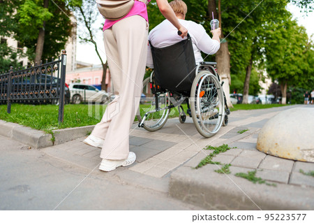 Back view of young woman helping mature woman in wheelchair in the city 95223577