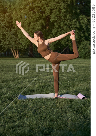 A young beautiful woman with a slim figure and long hair goes in for sports in the park on a warm summer day. 95223599