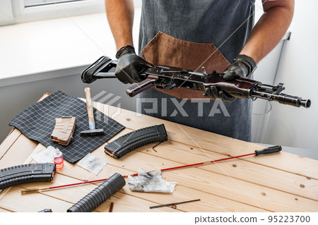 Close up of young man in apron disassembling a gun above the table 95223700