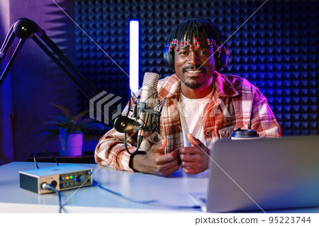 African radio host sitting at desk recording in studio with microphone and laptop African radio host sitting at desk recording in studio with microphone and laptop 95223744