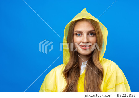 Young blonde woman wearing yellow raincoat smiling at camera over blue background in studio Young blonde woman wearing yellow raincoat smiling at camera over blue background in studio 95223855
