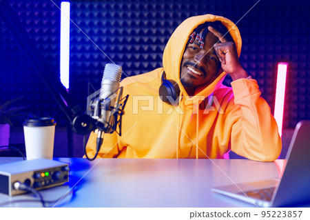 African radio host sitting at desk recording in studio with microphone and laptop African radio host sitting at desk recording in studio with microphone and laptop 95223857