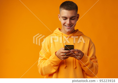 Portrait of a smiling young man holding mobile phone on yellow background 95223918