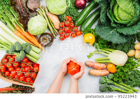 Healthy eating concept. Child's hands holding tomato. Organic vegetables broccoli cauliflower carrots kale pak choy onions. Healthy local farm produce on white wooden table, top view, selective focus Healthy eating concept. Child's hands holding tomato. Organic vegetables broccoli cauliflower carrots kale pak choy onions. Healthy local farm produce on white wooden table, top view, selective focus 95223943