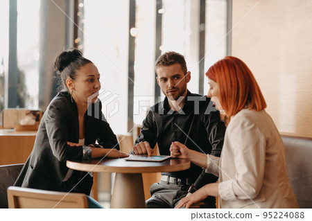 Business people in formal wear sitting coffee and analyzing data. On desk are laptops, graphs, tablets and paperwork. Business people in formal wear sitting coffee and analyzing data. On desk are laptops, graphs, tablets and paperwork. 95224088
