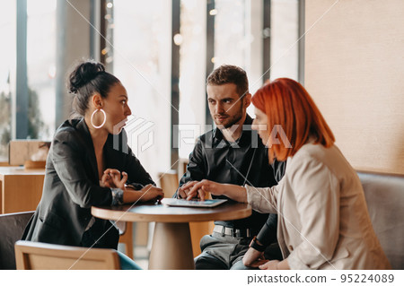 Business people in formal wear sitting coffee and analyzing data. On desk are laptops, graphs, tablets and paperwork. Business people in formal wear sitting coffee and analyzing data. On desk are laptops, graphs, tablets and paperwork. 95224089