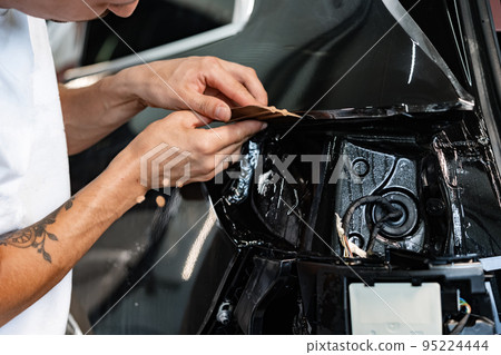 Close up of car wrapping specialist putting protective film on a car in detailing service 95224444