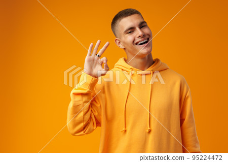 Happy young man gesturing OK sign against yellow studio background Happy young man gesturing OK sign against yellow studio background 95224472