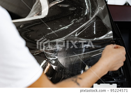 Car wrapping specialist wraps a car with adhesive film in car detailing service Car wrapping specialist wraps a car with adhesive film in car detailing service 95224571