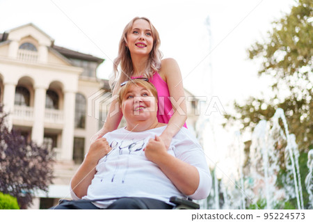 Young daughter taking care of her mother with disability sitting in wheelchair Young daughter taking care of her mother with disability sitting in wheelchair 95224573