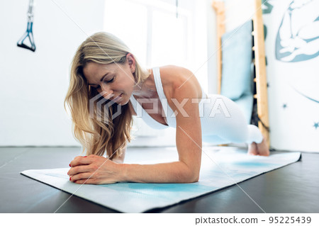 Middle-aged woman stretching on exercise mat at a gym. 95225439