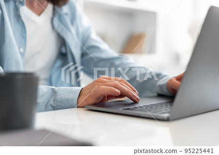 Close up shot of a man sitting at the table and working on laptop at home Close up shot of a man sitting at the table and working on laptop at home 95225441
