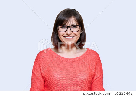 Smiling middle aged female looking at camera on light studio background Smiling middle aged female looking at camera on light studio background 95225442
