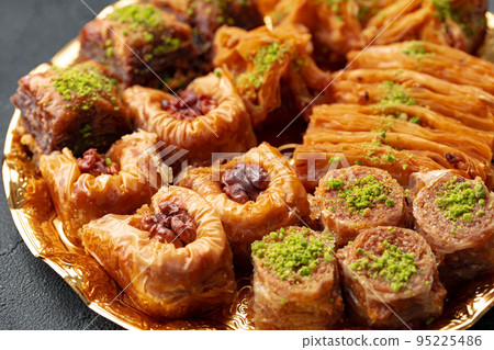 Delicious baklava dessert in oriental setting on black background Delicious baklava dessert in oriental setting on black background 95225486