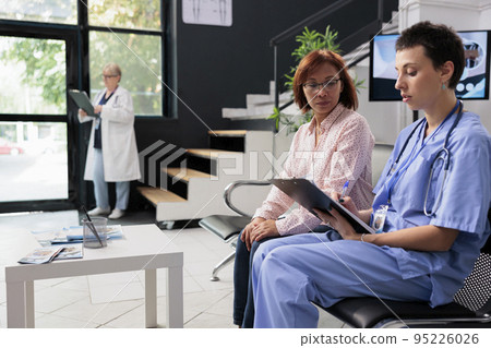 Medical nurse filling in report papers with asian patient, doing healthcare consultation hospital waiting room. Assistant writing checkup form documents before appointment. Medicine concept 95226026