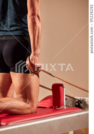 Handsome pilates male instructor performing stretching balance fitness exercise on small barrel equipment, at the pilates studio modern onterior indoor. Handsome pilates male instructor performing stretching balance fitness exercise on small barrel equipment, at the pilates studio modern onterior indoor. 95226292