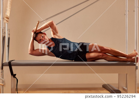 Fit man doing a lunge stretch yoga pilates exercise to strengthen and tone his muscles using a reformer in a gym 95226294