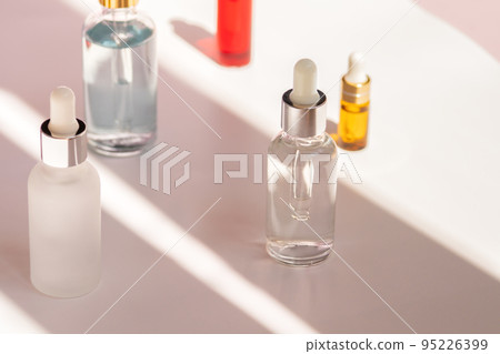Different glass dropper bottles with face serum, natural oil and anti-age moisturizer in sunny room. Skincare, facial and body cosmetics concept. High contrast photo, front view 95226399