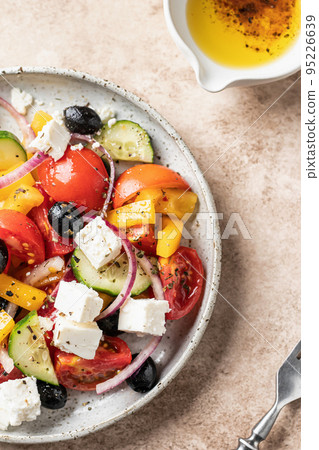 Traditional greek salad with feta cheese, tomatoes, red onion, cucumber, pepper, olive oil and italian herbs served on beige background. Close up, top view, flat lay Traditional greek salad with feta cheese, tomatoes, red onion, cucumber, pepper, olive oil and italian herbs served on beige background. Close up, top view, flat lay 95226639