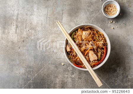 Funchose salad with chicken and vegetables in bowl with wooden chopsticks on green background, top view with text space. Asian food menu 95226643
