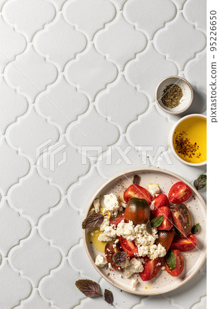 Salad with tomatoes, feta cheese and bazil leaves served for dinner on white tile background top view with copy space 95226650