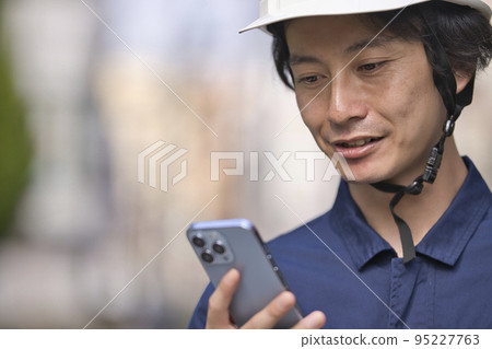 A man in work clothes looking at a smartphone in front of a construction site 95227763