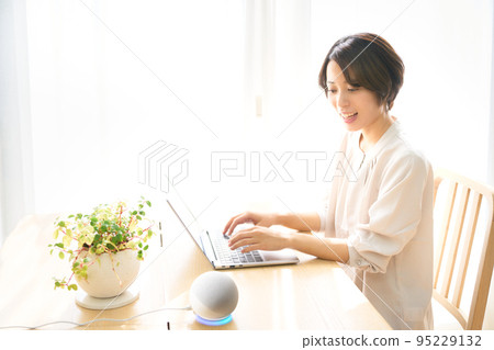 A young woman talking to an AI speaker while working on a PC 95229132