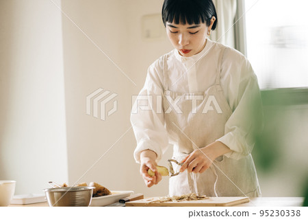 Woman peeling potatoes in the kitchen Woman peeling potatoes in the kitchen 95230338