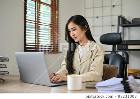 Confident Asian businesswoman concentrating on her work on laptop computer Confident Asian businesswoman concentrating on her work on laptop computer 95231008